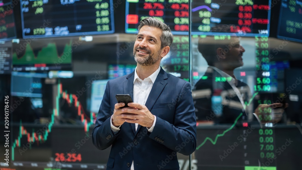 Fototapeta premium Happy businessman looking at stock market data on a mobile phone screen