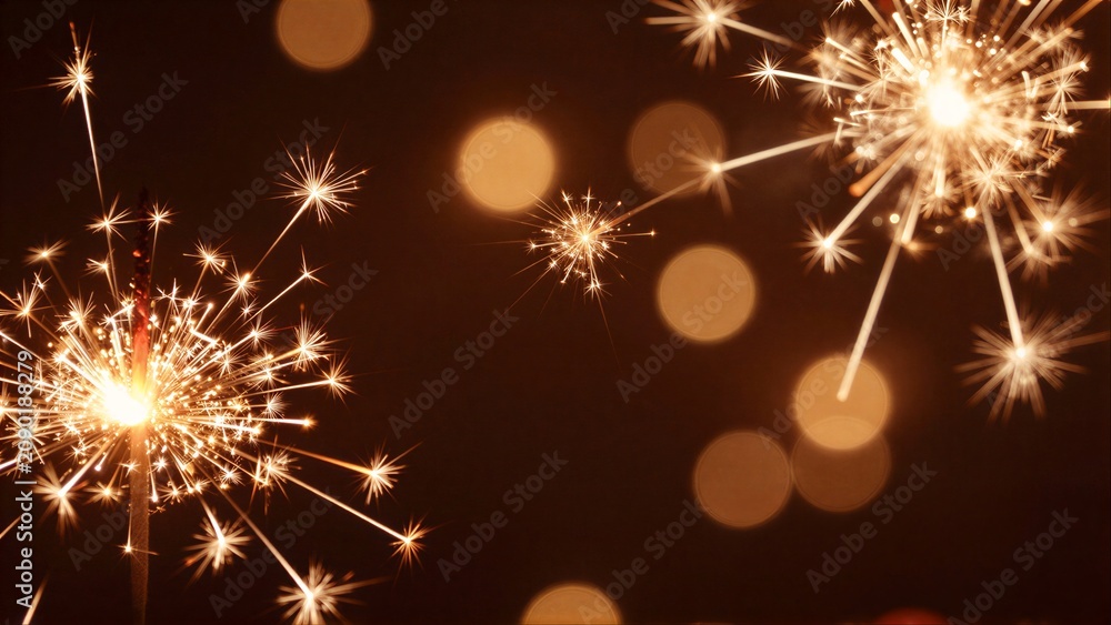 Fototapeta premium Golden sparklers burst in darkness, creating warm, festive light against a blurred night backdrop.