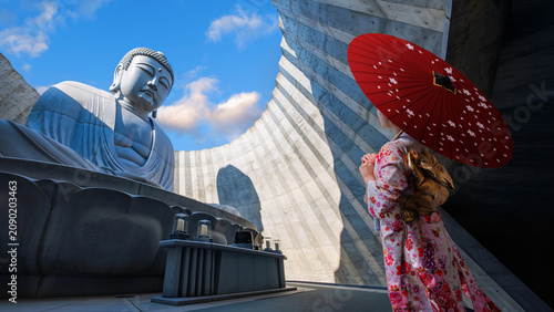 Young Japanese woman in a traditional Kimono dress with the Giant Buddha statue at  Makomanai Takino Cemetery in Sapporo, Hokkaido, Japan