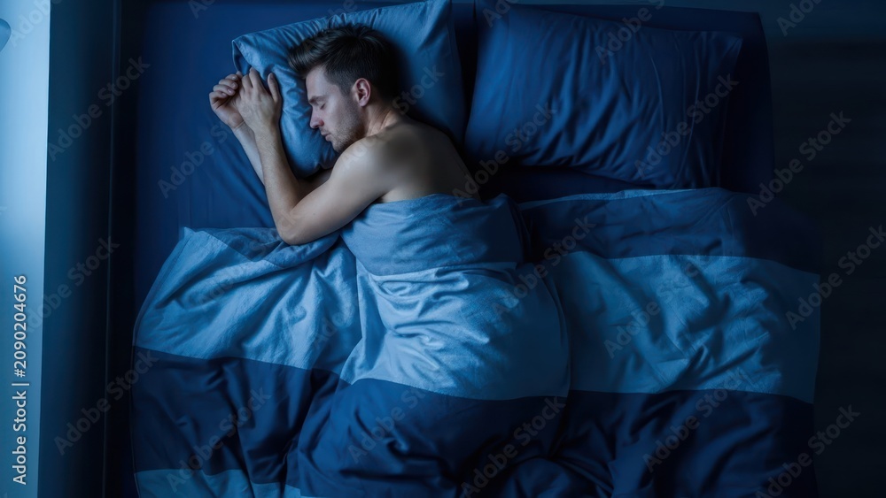 Obraz premium Man sleeping peacefully in dark bedroom, tranquil night rest, comfortable bed