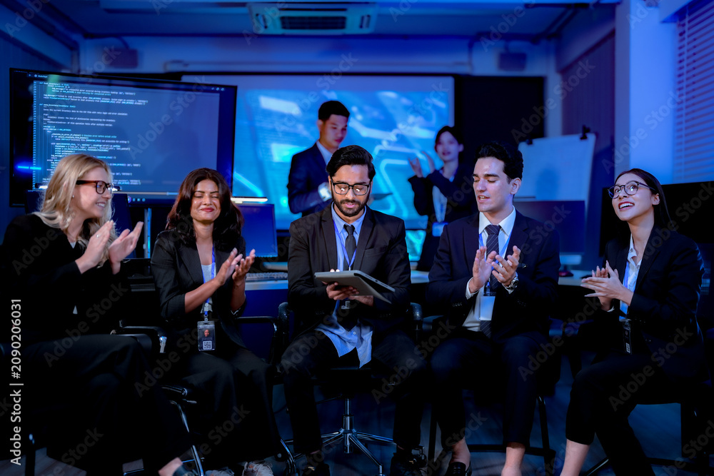 Obraz premium Delighted colleagues applauding and raising arms during a team win toasting without glasses in a dark blue technology office at night during a busy working session.