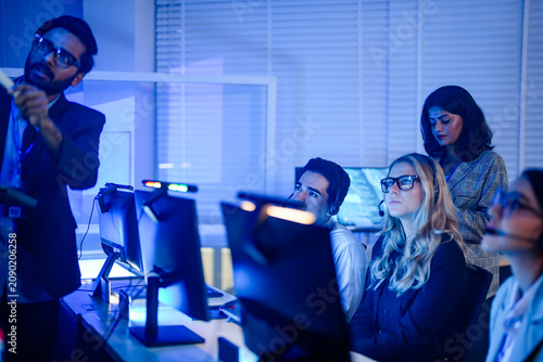 Headset wearing agents raising hands during a floor training session asking about the new tool in a bright open plan support office captured in an authentic working moment.