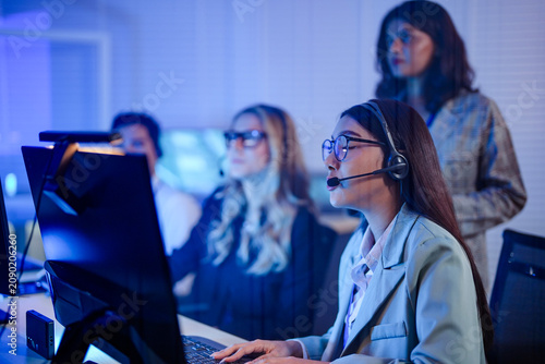 Foto Female trainer standing behind seated agents in headsets at their screens guiding the new hire's first call colleagues at a flipchart in the bright office behind at work