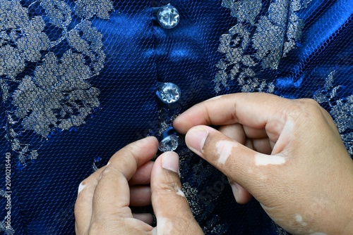 Принти на полотні A woman's hands fastening the buttons on a brocade garment.