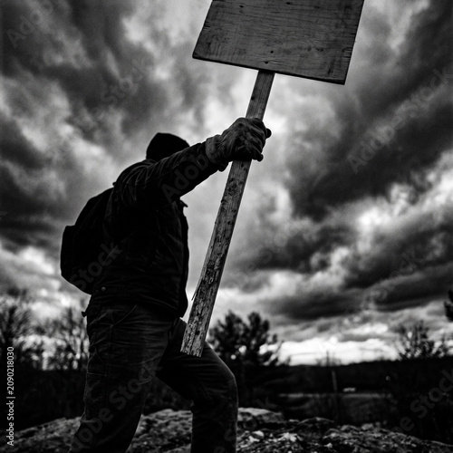 Person holding blank sign against stormy sky, protest, activism, black and white