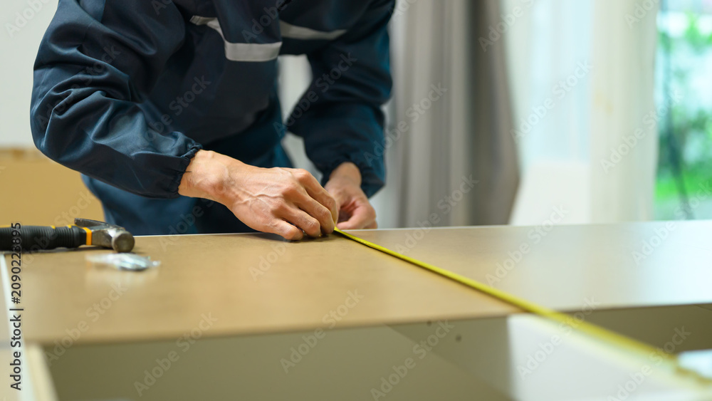 Fototapeta premium Worker in uniform measuring wooden board with tape measure during furniture assembly or home renovation