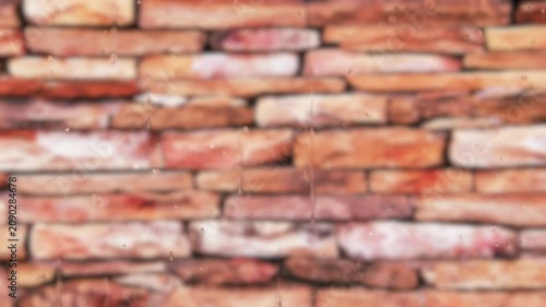 Clear rain drops and trickling water streaks stream down a transparent glass pane overlooking a soft blurry out of focus stacked red stone wall background on a stormy day