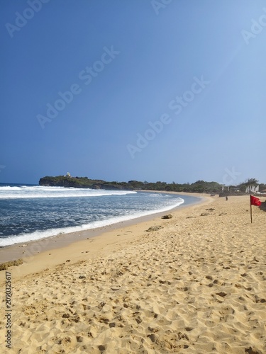 Beautiful sandy beach shoreline with blue ocean waves and foam on sunny day