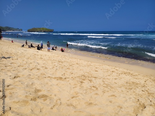 Beautiful sandy beach shoreline with blue ocean waves and foam on sunny day