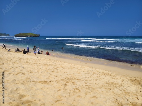 Beautiful sandy beach shoreline with blue ocean waves and foam on sunny day