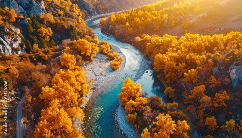 Aerial view of a winding river flowing through a valley filled with vibrant autumn foliage and rocky mountains under warm sunlight.