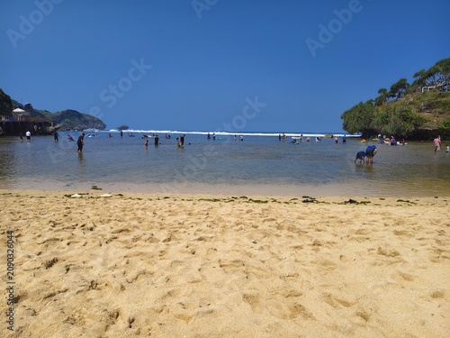 Beautiful sandy beach shoreline with blue ocean waves and foam on sunny day