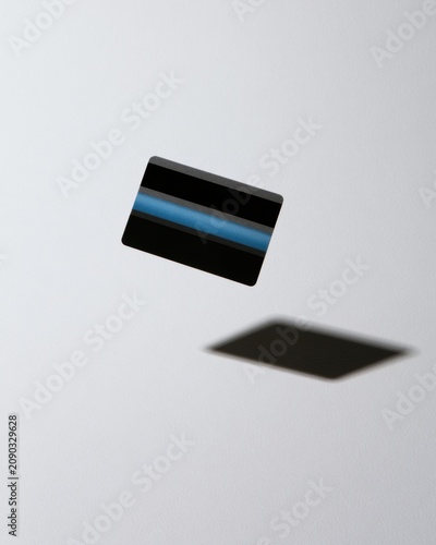 A credit card is frozen in the air with motion blur on a white surface, casting a crisp shadow below it. The setting shows a studio approach.