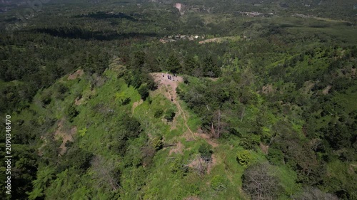 4k aerial drone video footage of Mount Merapi volcano seen from Klangon Hills emitting volcanic smoke from its summit crater, surrounded by forest mountain ridges, clear blue daytime sky.