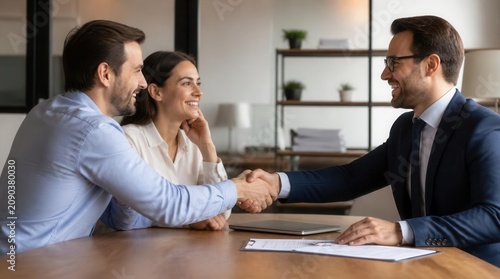 Professional financial advisor warmly shaking hands with a happy couple seated at a desk during a consultation, discussing plans and agreements with smiles and positive interactions signifying