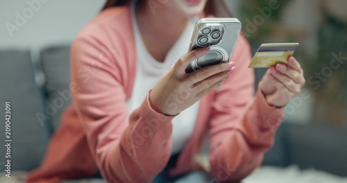 Close-up of Asian woman typing on smart phone while holding credit card to buy product online at home.
