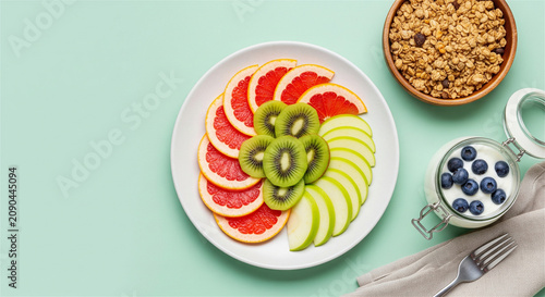 Healthy breakfast fruit platter with sliced grapefruit, kiwi and apple. Yogurt with blueberries and granola bowl on mint background. Nutritious morning meal.