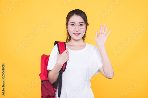 Smiling young student with backpack waving on yellow background