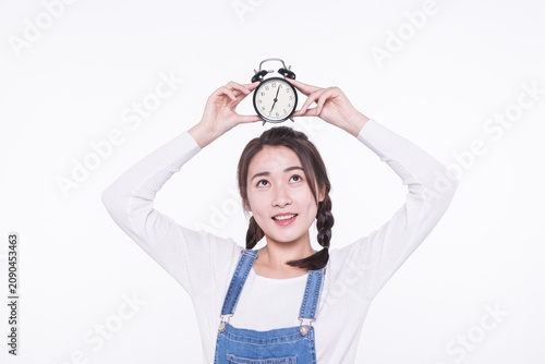 Young woman holding alarm clock above her head on white background