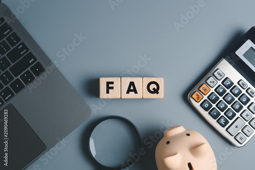 Wooden blocks spelling FAQ (Frequently Asked Questions) on grey office desk workspace with finance tools. concept of finding financial answers and customer support