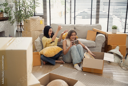 Cheerful Asian woman throw white foam peanut to playful friend while unpack cardboard box in living room. Fun family lifestyle on moving day to new house concept