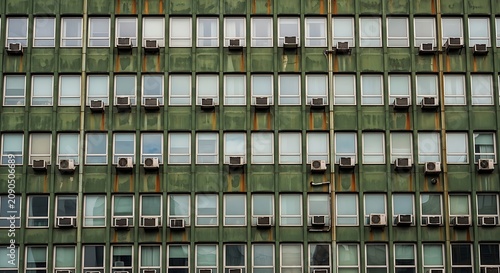 Weathered Green Apartment Building Facade with Repeating Windows and Air Conditioners