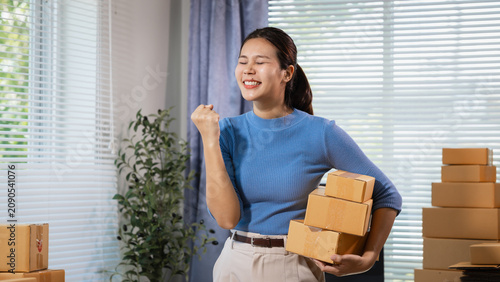 Foto Smiling young woman holding cardboard boxes at home office, celebrating success in small business shipping and online selling