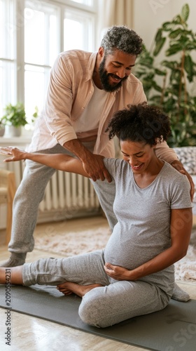 Pregnant woman stretches on yoga mat with partner assisting indoors