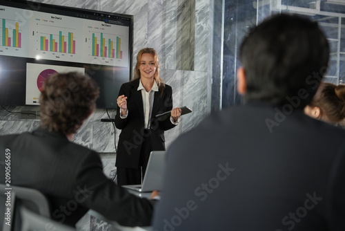 Fotografie Smiling brightly, the presenter opens both hands wide as she lands a persuasive line, her tablet and pen catching the light in the dim marble meeting room in a bright modern coworking