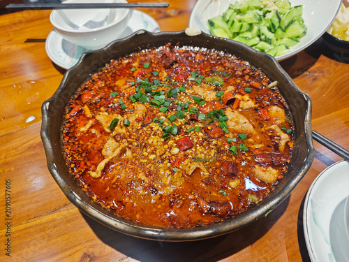 A large bowl of spicy Sichuan boiled meat covered in red chili oil, peppercorns, and fresh green scallions