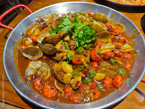 A savory seafood dish featuring stir-fried crayfish and clams with garlic, chili, and fresh cilantro, served in a metal pan
