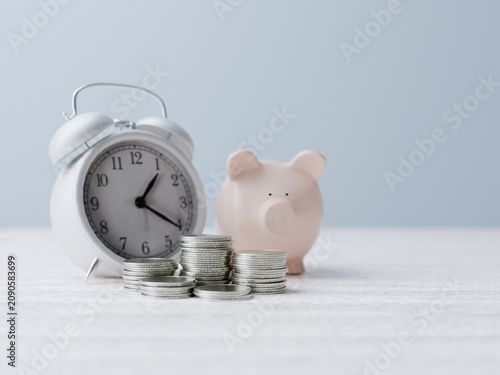 Foto Piggy bank and stacked coins resting near a vintage alarm clock on a wooden tabl
