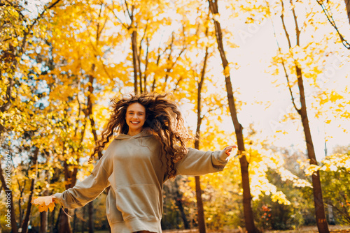Konstfotografi Smiling young woman plays and jumping in the autumn park with the yellow leaves at sunset