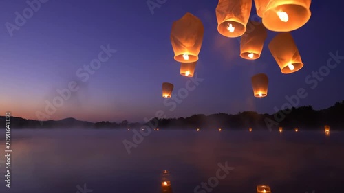 Warm paper lanterns drifting up into a twilight sky over calm water