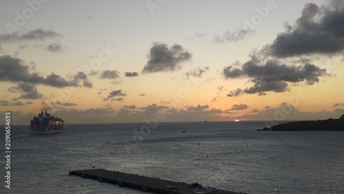 Photography A cruise ship sailing across the ocean at sunset beneath a dramatic sky with scattered clouds
