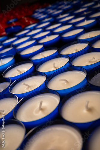 Rows of unlit red and blue votive candles on a stand. High angle close-up shot of white wax and wicks in glass cups, creating a repeating pattern.