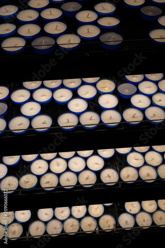 Rows of unlit red and blue votive candles on a stand. High angle close-up shot of white wax and wicks in glass cups, creating a repeating pattern.