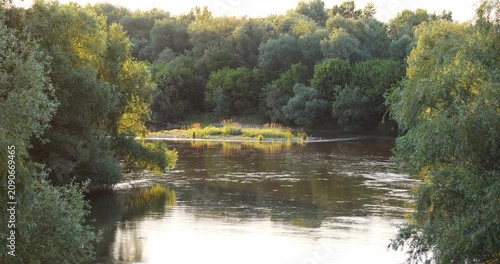 Scenic static shot of a calm river flowing through a lush green forest at sunset with reflections