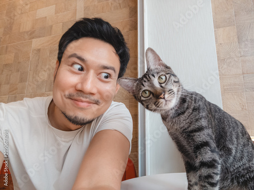 Funny Man Takes Selfie with Curious Tabby Cat, Sharing a Playful Moment Indoors
