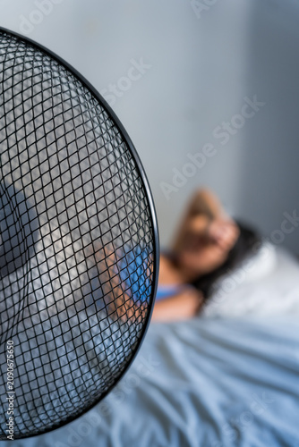 out of focus unrecognizable woman in bed during a hot summer heat wave with fan, cooling off fighting heat at home during a heatwave and high temperature, vertical