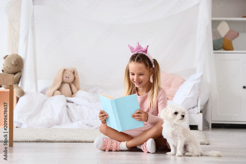 Obraz premium Cute little happy girl in princess crown with Maltese dog reading book on floor at home