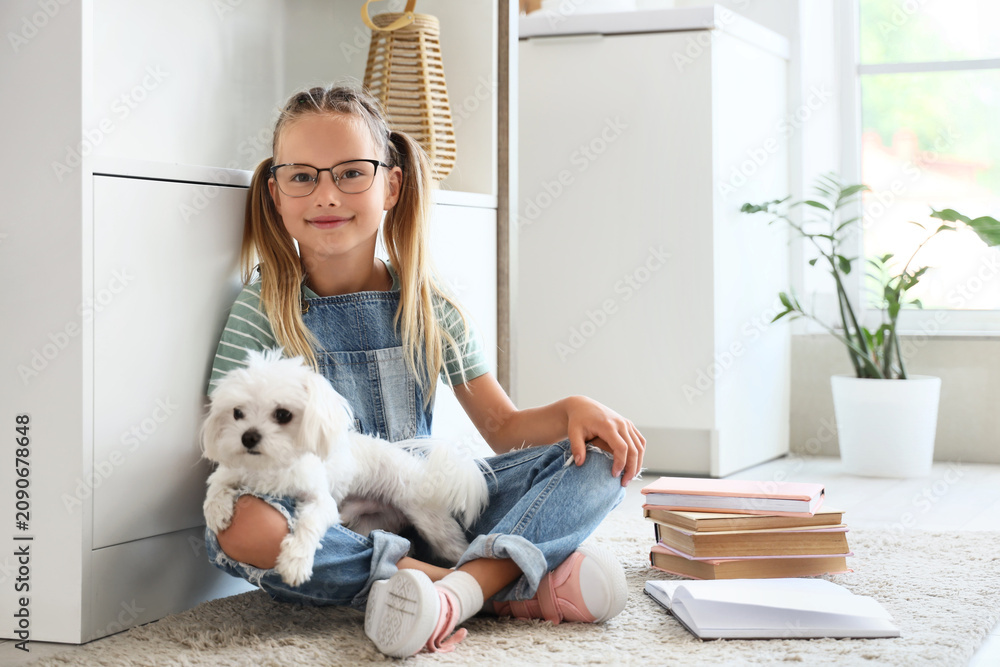 Obraz premium Cute little happy girl with Maltese dog and many books sitting on floor in kitchen