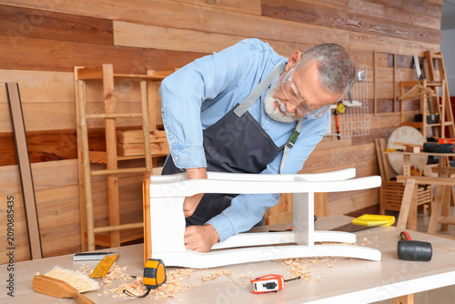 Fotografie Mature carpenter working with wooden table in shop
