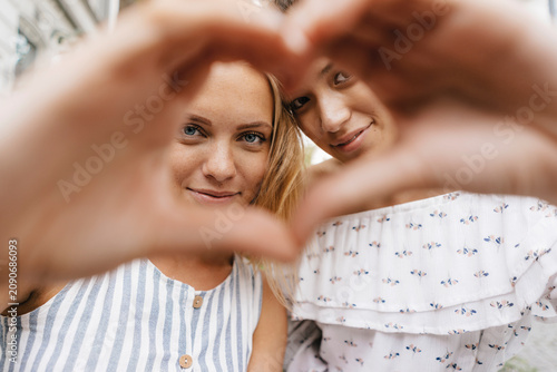 Two smiling young women shaping heart with their hands