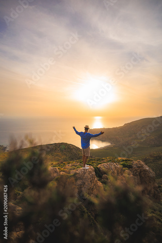Traveler with open arms stands on a rocky cliff above the western coast of Crete