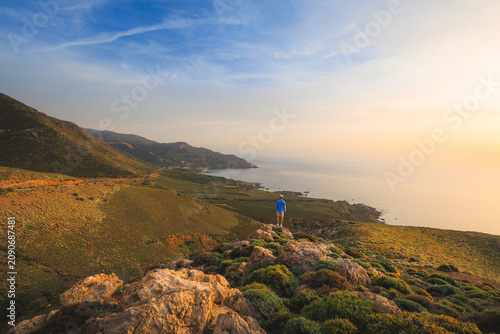 Lone traveler watches sunset above the western coast of Crete, surrounded by rocky hills
