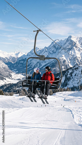 Skiers riding a chairlift on a sunny winter day with groomed ski slopes and a beautiful mountain resort backdrop, minimalist outdoor winter sports concept