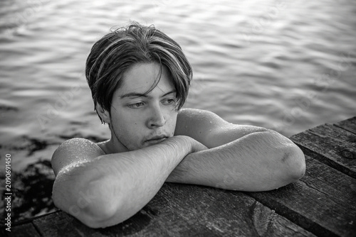 Tableau sur toile Thoughtful and melancholic portrait of a teenage boy leaning on a wooden pier in