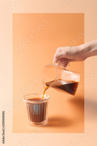Hand pours black coffee into a glass cup prepared brewing method with filter against paper background with text space. Alternative coffee brewing method with filter