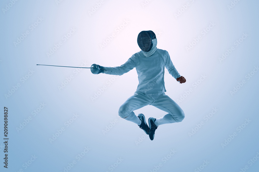 Fototapeta premium Male fencer jumping with epee during dynamic fencing action. Concept of explosive movement, athletic agility, sports performance, competitive fencing, and action photography.